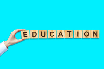 Education concept. Female hand makes up Word out of the alphabet on wooden blocks. Blue background....