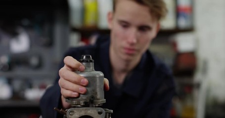 4K Confused trainee mechanic examining vehicle parts in auto repairs shop
