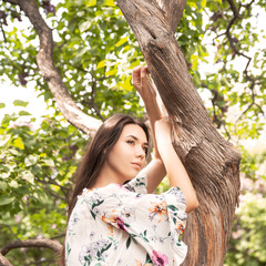 Portrait of young beautiful woman wearing a white blouse. Big tree in the park. Perfect body shape. Fashion portrait.