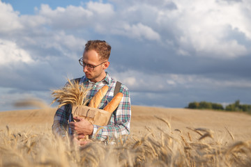 Male farmer or baker with baguettes in rye, wheat field