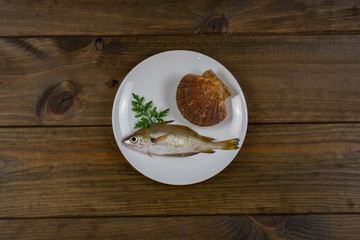 Pescado con vieira fresca y perejil con limones sobre plato blanco y mesa de madera oscura con utensilios de madera