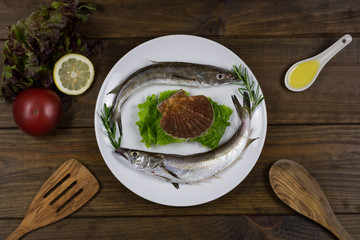 Pescadillas frescas con limones sobre plato blanco y mesa de madera oscura con utensilios de madera
