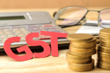 The word GST from paper letters and coins and a calculator on a natural wooden table. Taxes