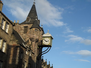 Clock at a medieval Scottish castle architecture showing the time with blue sky and scattered clouds background
