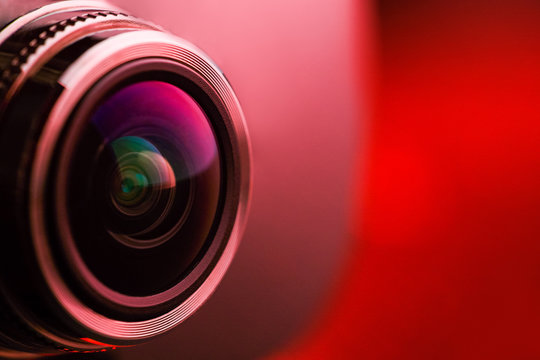 Camera lens with red backlight. Side view of the lens of camera on red background. Red  camera Lens close Up. Pure red