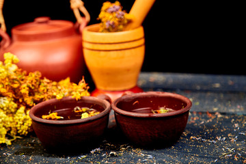 Cup of herbal tea - tutsan, sagebrush, oregano, helichrysum, lavender near brown teapot on dark wooden background. Herbal tea. Dry Herbs and flowers, herbal medicine. .