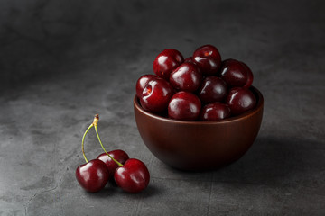Ripe and juicy cherry berries on a black textural background in a brown cup, with water drops. Top view, close-up.