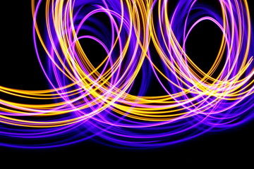 Long exposure photograph of neon purple and metallic gold colour in an abstract swirl parallel lines pattern against a black background. Light painting photography.