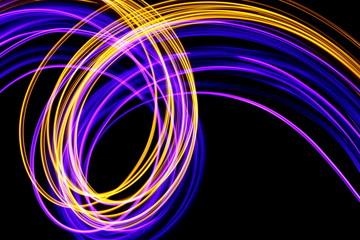 Long exposure photograph of neon purple and metallic gold colour in an abstract swirl parallel lines pattern against a black background. Light painting photography.