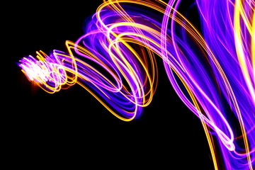 Long exposure photograph of neon purple and metallic gold colour in an abstract swirl pattern against a black background. Light painting photography.