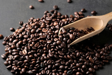 Roasted coffee grains and a wooden spoon on a black background. close-up. Rabusta, Arabica.