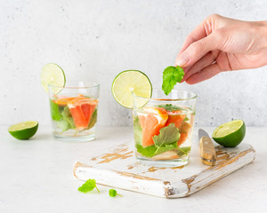 Fototapeta premium Hand laying a leaf of mint in glass of cool infused water with fresh grapefruit, lime, (lemonade, cocktail). Detox drink, health care, fitness, diet concept.