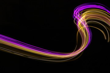 Long exposure photograph of neon purple and gold colour in an abstract swirl parallel lines pattern against a black background. Light painting photography.
