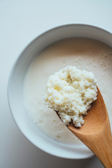 Close up of kefir grains being strained on the wooden spoon