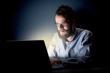 Young handsome businessman working late at night in the office with a dark background