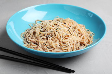 Plate of noodles with sesame and chopsticks on table, closeup
