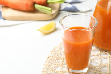 Glass of fresh carrot juice on white wooden table, space for text