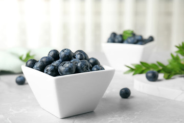 Bowl of tasty blueberries on grey table, space for text