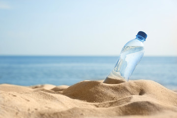 Sandy beach with bottle of refreshing drink on hot summer day, space for text