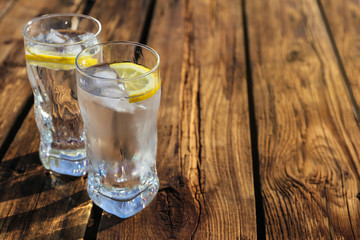 Glasses of refreshing drink with ice and lemon for hot summer day on wooden table, space for text
