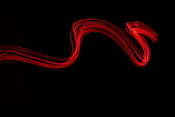 Long exposure photograph of neon red colour in an abstract streak pattern against a black...