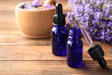Bottles with natural lavender oil, dropper and flowers on wooden table, closeup view. Space for text