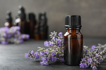 Obraz na płótnie Canvas Bottle with natural lavender oil and flowers on wooden table against grey background, closeup view. Space for text