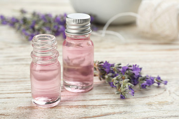 Fototapeta na wymiar Bottles with natural lavender oil and flowers on white wooden table, closeup view. Space for text