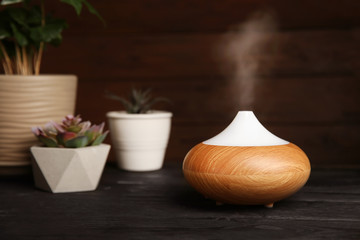 Composition with modern essential oil diffuser on black wooden table against dark background, space for text