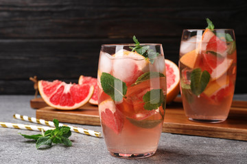 Glass of refreshing drink with grapefruit and mint on grey stone table against dark background, space for text