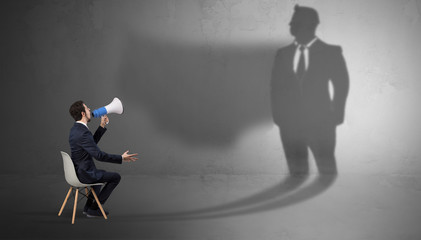 Humble businessman staying and offering stuffs to a huge businessman shadow