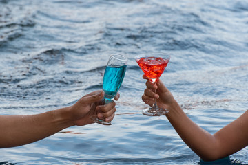 Young couple holding a glass of wine at swimming pool on vacation.