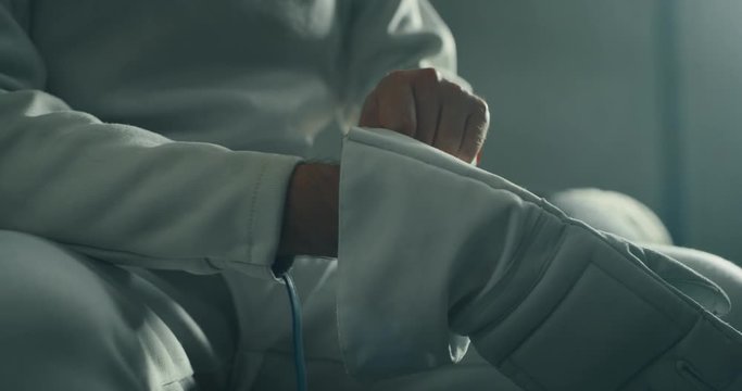Cinematic slow motion close up of young man fencer is putting on a professional equipment before start a practising assaults of fencing with rapier in a gym.