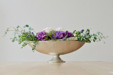 bouquet of green white and purple flowers in a silver metal bowl on a table bucket white background