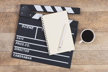 Movie clapper with paper, pen and cup of coffee on wooden planks background