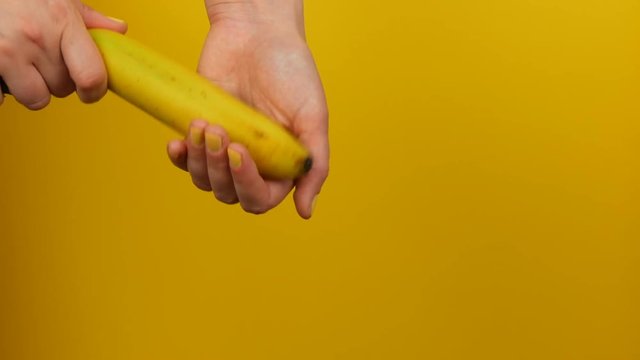 Female hand with yellow manicure holds a ripe banana fruit on a yellow background