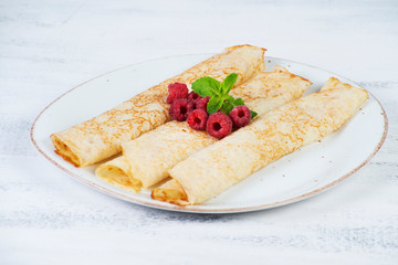 Thin pancakes for Breakfast on a plate with raspberry jam on a light background