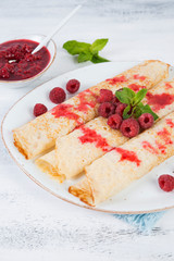 Thin pancakes for Breakfast on a plate with raspberry jam on a light background