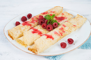 Thin pancakes for Breakfast on a plate with raspberry jam on a light background