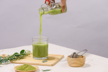 Green tea being poured into glass tea cup on white table