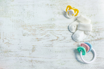 Baby accessories for newborns: socks, toy and soother on light wooden background. Motherhood...