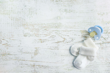 Baby accessories for newborns: socks and soother on light wooden background. Motherhood concept....