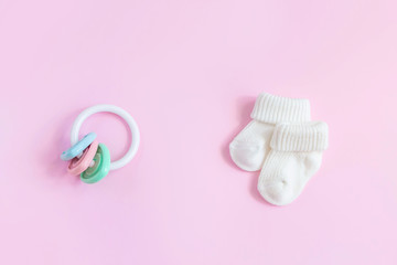 Baby accessories for newborns: socks and toy on  pink background. Motherhood concept. Top view, flat lay composition.