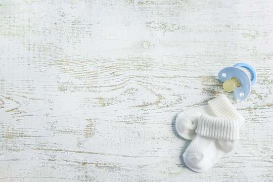 Baby accessories for newborns: socks and soother on light wooden background. Motherhood concept. Top view, flat lay composition. Copy space for text.