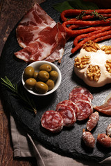 Cutting board with prosciutto, salami, cheese,bread and olives on dark stone background