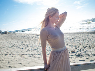 Young cheerful girl on the seashore. Young blonde woman smiling. Trendy beige skirt