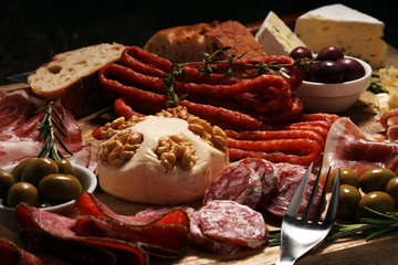 Cutting board with prosciutto, salami, cheese,bread and olives on dark wooden background
