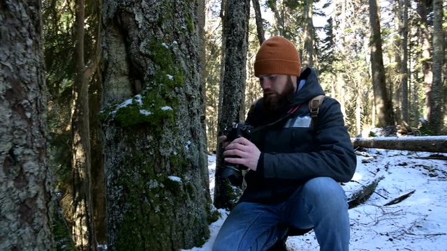 A bearded male traveler photographer with his camera in the winter forest takes pictures of nature. Travel concept for bloggers and photo artists