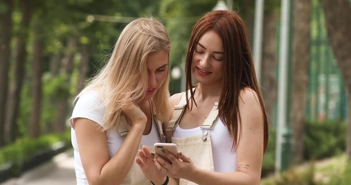 Two happy women friends sharing social media in a smart phone outdoors in a park