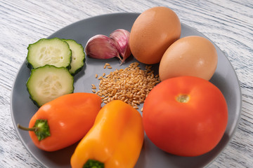 garlic, pepper, tomato, flax seeds, cucumber, chicken eggs on a gray plate